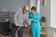Senior man shows photos of his family with grandchildren to friendly nurse at retirement home. Old man with walking stick and smiling young woman in uniform scrubs looking at mobile phone together