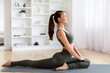 © Prostock-studio - Beautiful young Asian woman practicing yoga in pigeon pose at home