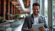 © SS Digital - A young, prosperous Hispanic man uses a tablet computer app at work. He smiles and works with a laptop while wearing a business suit. He is delighted with his accomplishment