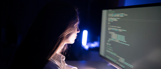 a focused woman works diligently on her coding assignment in front of a computer screen in a dimly l