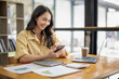 © Wasana - Attractive Asian businesswoman sitting using mobile phone at table in office