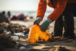 woman in orange gloves picking up plastic bottles on the beach