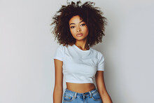Young Beautiful African American Woman With Curly Hair In White T Shirt Posing With Blue Jeans Isolated On Light Grey Background