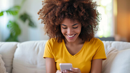 Wall Mural - young woman with curly hair, wearing a yellow shirt, smiling and looking down at her smartphone