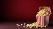 Delicious popcorn spilled from a red striped cardboard box on a dark red background with copy space