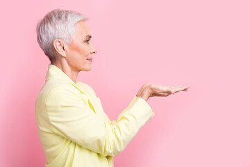 Side photo of mature cheerful marketing manager lady hold arms introduce benefits cooperation with her isolated on pink color background