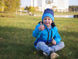 Little happy boy in a blue jacket and hat having fun in the spring on the lawn