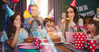 Caucasian small cute birthday boy blowing the candles on he cake while his happy friends in colorful conuses applauding and smiling. Birthday party for children.