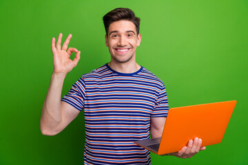 Sticker - Portrait of friendly guy toothy smile hold netbook demonstrate okey symbol isolated on green color background