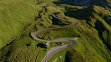 Breathtaking Mountain Road. A Cinematic Aerial Shot Of A Car Driving On An Empty Twisty Alpine Road During Golden Hour, Surrounded By Greenery. Concept Of A Road Trip And Luxury Travel.