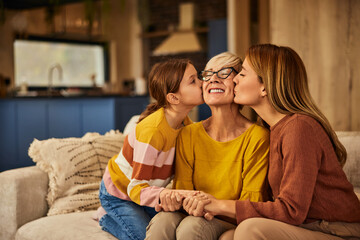 Wall Mural - Happy grandma getting kisses from her daughter and grandchild, sitting on the sofa.