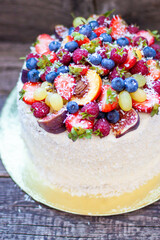Wall Mural - Coconut cake with a pile of fresh peaches, apples, raspberries, blueberries and nuts on wooden background