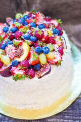 Wall Mural - Coconut cake with a pile of fresh peaches, apples, raspberries, blueberries and nuts on wooden background