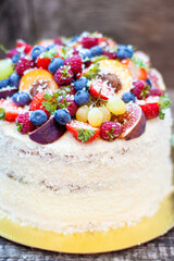 Wall Mural - Coconut cake with a pile of fresh peaches, apples, raspberries, blueberries and nuts on wooden background