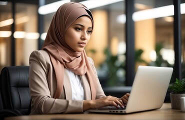 Young muslim woman wearing hijab sitting working with laptop computer in her modern business office