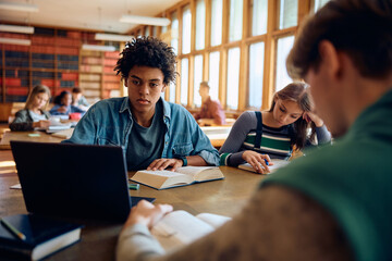 Black student and his friends learning in library at high school.