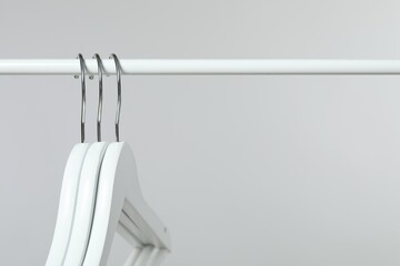 Sticker - Empty clothes hangers on rack against light grey background, closeup. Space for text