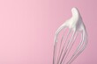 Whisk with whipped egg whites on pink background, closeup. Space for text