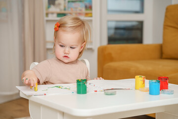 Child baby toddler girl paints with finger paints and gets her hands dirty