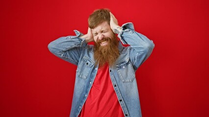 Poster - Stressed young redhead man tiredly covering ears over noisy anxiety, isolated on red background, expressing emotional headache problem