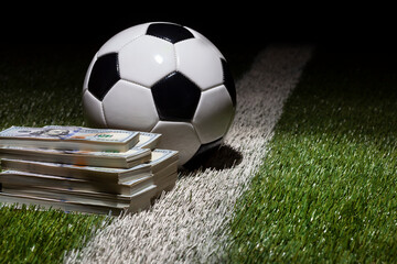 Poster - Soccer ball on grass field with stripe by stacks of one hundred dollar bills