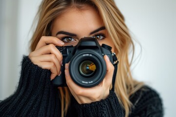 Wall Mural - Crop smiling female in black sweater looking at camera while taking photo on professional digital camera in house on white background