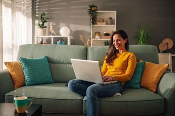 portrait of a woman using laptop while sitting on a mint couch at home
