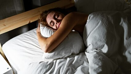 Poster - A peaceful young woman sleeping soundly in a cozy, dimly-lit bedroom, embracing a pillow.