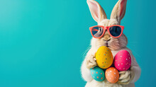 An Easter Bunny Rabbit Wearing Sunnies, Shades, Sunglasses Holding Colourful Easter Eggs Against A Turquoise Isolated Background With Room For Text.
