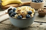 Fototapeta Mapy - Tasty oatmeal with banana, blueberries and walnuts served in bowl on wooden table