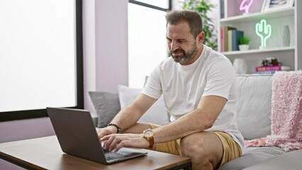 Wall Mural - Mature man with grey hair using laptop at home, depicting remote work in a comfortable living room setting.