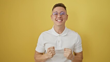 Wall Mural - Triumphant young hispanic man in glasses celebrates a joyful victory, standing against an isolated yellow background, exuding confidence and happiness.