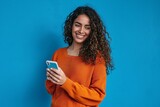 Fototapeta  - Young adult smiling happy pretty latin woman holding mobile phone device, doing ecommerce online shopping on cell, using apps on cellphone standing isolated on blue, Generative AI