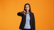 Asian female model giving dislike in front of camera, showing thumbs down with displeased facial expressions. Businesswoman does rejection and disapproval gesture over backdrop.