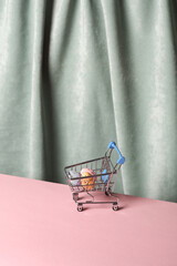 Wall Mural - Shopping trolley with easter eggs against the background of a curtain. Aesthetic still life. Minimalism. Holiday mood