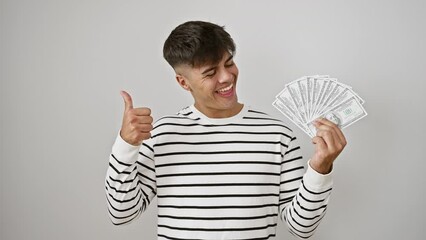 Canvas Print - Joyful young hispanic man confidently showing off handfuls of dollar banknotes. gesturing approval sign, his beaming smile reflects success. isolated on a pristine white background.