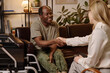 © AnnaStills - Joyful black man with disability shaking hands with female psychologist sitting on sofa at office