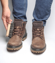 Wall Mural - Man cleaning with brush leather boots on a white background