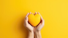 Female hands on a yellow background holding a yellow heart. The concept of donations and family insurance, World Heart Day. Valentine's Day.