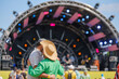 © Anton Gvozdikov - A loving couple hugs and dancing enjoying the ambiance in front of a festival music stage on a sunny day.