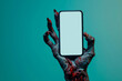 Creepy halloween monster zombie hand holding a mobile phone with a blank screen