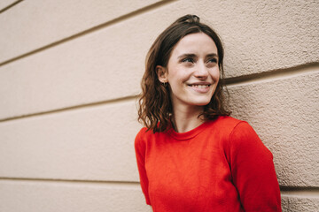 joyful young woman leaning against urban building, laughing sideways