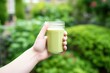 hand holding iced matcha latte with green garden background