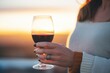 womans hand holding a glass of merlot at sunset