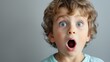 Shocked or surprised and startled four year old preschool little caucasian boy in awe left speechless with his eyes and mouth wide open on neutral background