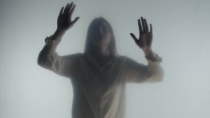 silhouette of panicked woman in fog behind frosted glass or curtain. the woman is tapping her palms 