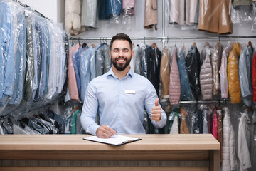 Wall Mural - Dry-cleaning service. Happy worker showing thumb up at counter indoors