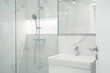 A modern, bright bathroom with marble walls, a glass shower with a silver shower head, and a white sink with a silver faucet.