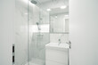A Modern, bright bathroom with white marble walls, a glass shower, and a sleek sink under a large mirror.