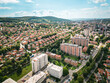 Zlin’s cityscape with a blend of urban structures and green spaces, with forested hills in the distance. There is visible a typical sign of Zlin - buildings are made of orange bricks.